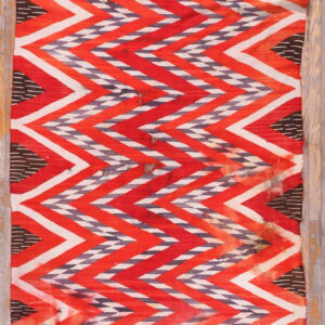 Red, white, and gray flatweave rug with a bold zigzag pattern rests on light wood plank flooring.