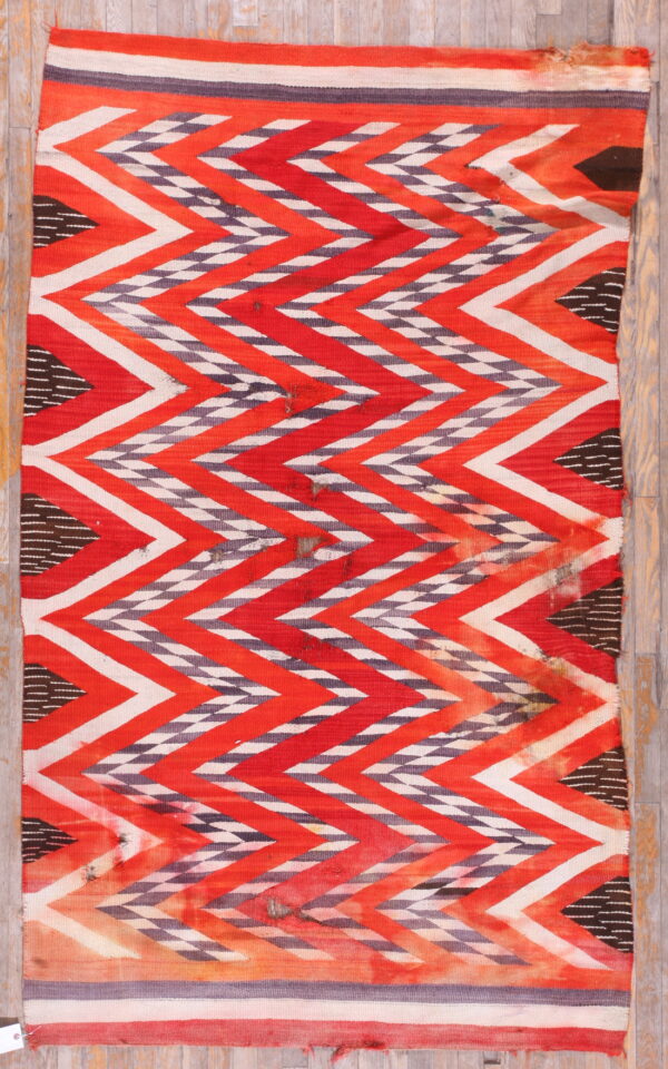 Red, white, and gray flatweave rug with a bold zigzag pattern rests on light wood plank flooring.