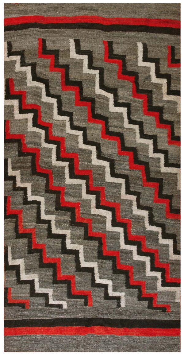 Low-pile rug with a dark gray field and diagonal stepped zigzag pattern in red, black, and off-white.