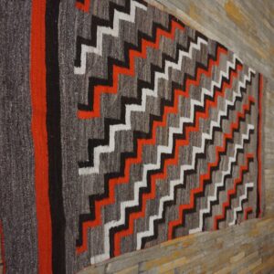 Gray, black, white, and bright orange zigzag runner rug displayed against distressed wooden planks.