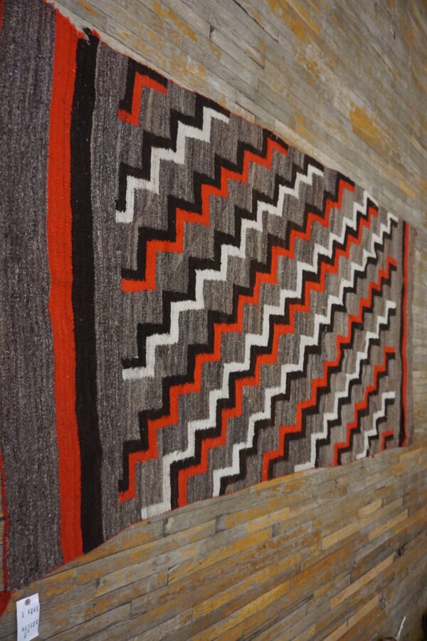 Gray, black, white, and bright orange zigzag runner rug displayed against distressed wooden planks.