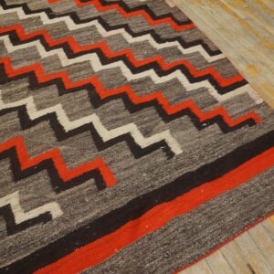 Rustic gray, red, white, and black zigzag rug resting on distressed wood planks with yellow undertones.