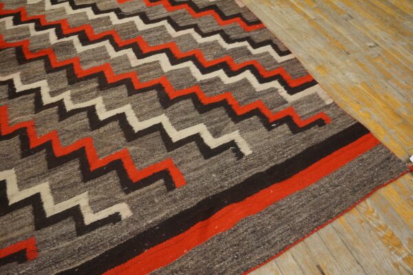 Rustic gray, red, white, and black zigzag rug resting on distressed wood planks with yellow undertones.