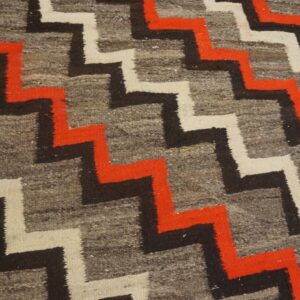 Geometric rug showing gray, red, black, and white stepped patterns next to light wood floorboards.
