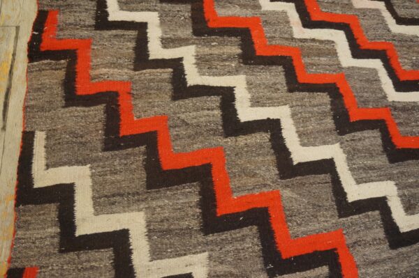 Geometric rug showing gray, red, black, and white stepped patterns next to light wood floorboards.