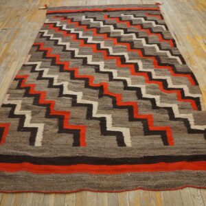 Stepped black, cream, and red zigzags cover a gray rug on worn wooden flooring.