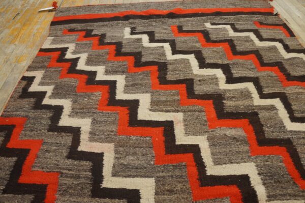 Low-pile rug with interlocking orange, black, and cream zigzag geometric patterns displayed on a wood floor.