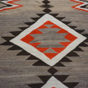 Geometric flatweave rug featuring sawtooth triangles and a large central diamond in orange, white, and natural tones.