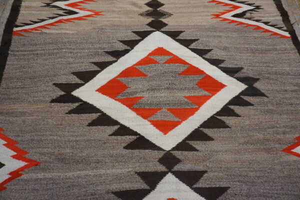 Geometric flatweave rug featuring sawtooth triangles and a large central diamond in orange, white, and natural tones.