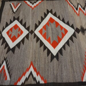 Geometric flatweave rug in gray, orange, white, and dark brown on a weathered wooden floor.