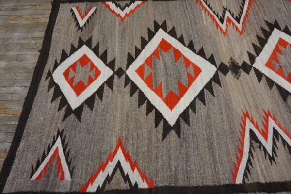 Geometric flatweave rug in gray, orange, white, and dark brown on a weathered wooden floor.