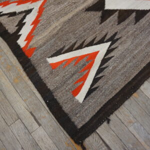 Geometric flatweave rug in gray, black, orange, and white shown closely on weathered gray hardwood flooring.