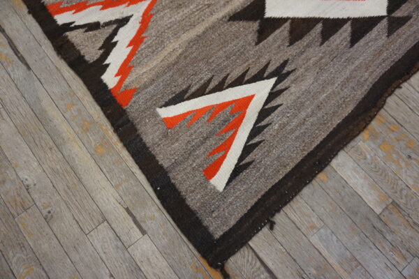 Geometric flatweave rug in gray, black, orange, and white shown closely on weathered gray hardwood flooring.