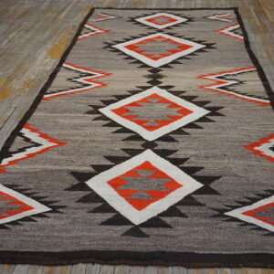A flatweave runner featuring gray, orange, black, and white geometric designs rests on worn wooden floors.