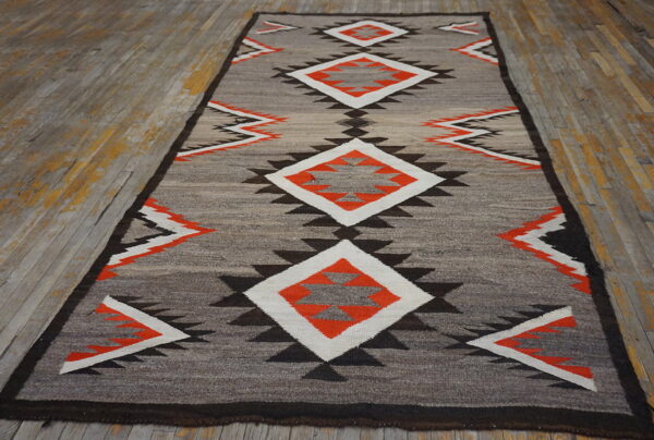 A flatweave runner featuring gray, orange, black, and white geometric designs rests on worn wooden floors.