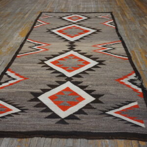 Narrow grey rug with central orange and white geometric diamonds on a weathered wooden floor.