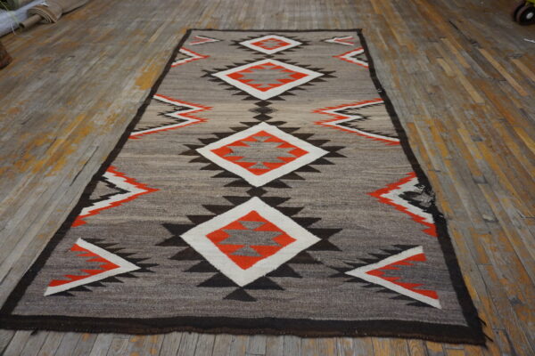 Narrow grey rug with central orange and white geometric diamonds on a weathered wooden floor.