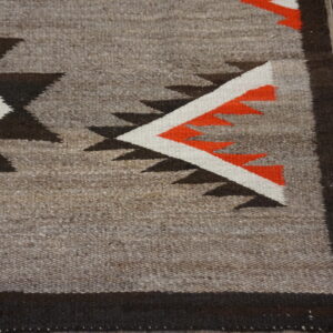 Geometric flatweave rug in gray, black, white, and bright orange colors on distressed wood planks.
