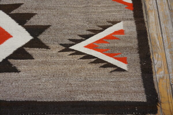 Geometric flatweave rug in gray, black, white, and bright orange colors on distressed wood planks.