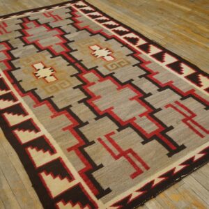 Geometric low-pile rug in grey, red, brown, and cream with stepped motifs on weathered wood floor.