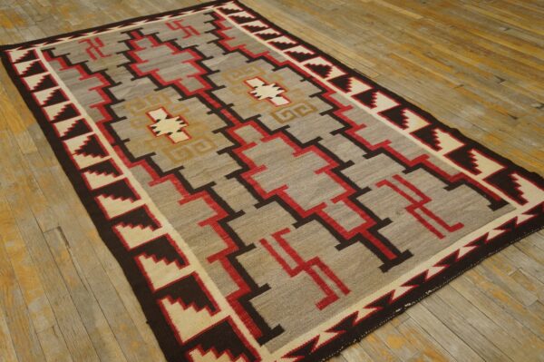 Geometric low-pile rug in grey, red, brown, and cream with stepped motifs on weathered wood floor.