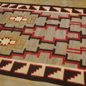 Gray flatweave rug with repeating stepped patterns and central medallions in red, brown, and cream.