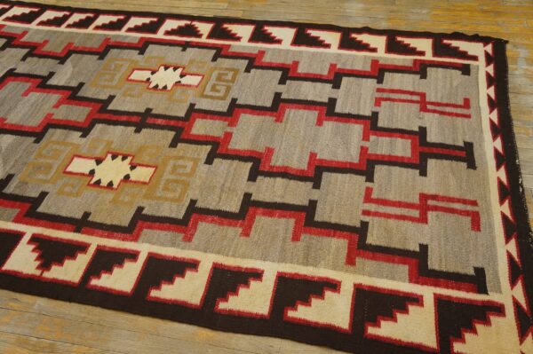 Gray flatweave rug with repeating stepped patterns and central medallions in red, brown, and cream.