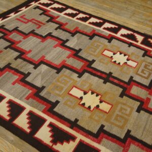 Geometric flatweave rug in gray, red, tan, and brown featuring zigzags and borders on wood planks.