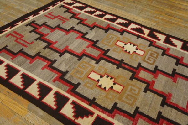 Geometric flatweave rug in gray, red, tan, and brown featuring zigzags and borders on wood planks.