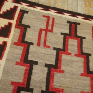 Geometric flatweave rug in grey, red, brown, and cream, angled on rustic wooden plank flooring.