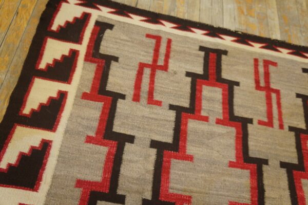 Geometric flatweave rug in grey, red, brown, and cream, angled on rustic wooden plank flooring.