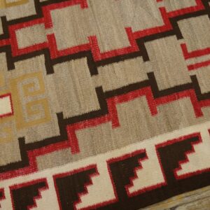 Beige flatweave rug with striking red, dark brown, and yellow stepped geometric designs on wood floor.