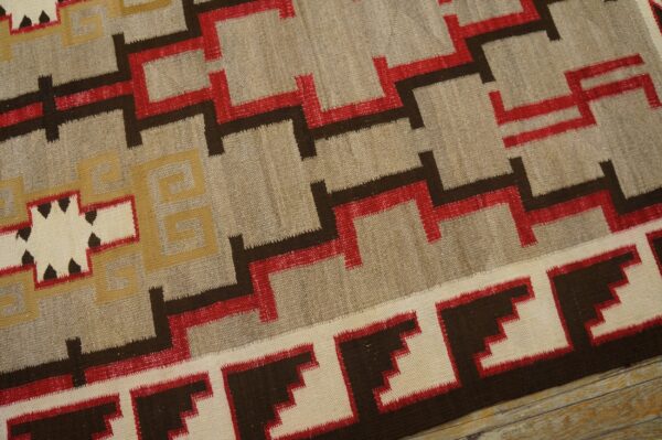 Beige flatweave rug with striking red, dark brown, and yellow stepped geometric designs on wood floor.