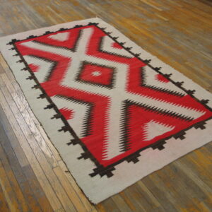 Flatweave rug with a red, cream, and brown serrated diamond pattern on distressed wood planks.