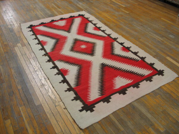 Flatweave rug with a red, cream, and brown serrated diamond pattern on distressed wood planks.
