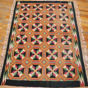 Geometric flatweave rug featuring repeating medallions in black, orange, green, and pink on plank wood flooring.