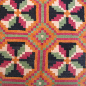 Geometric flatweave rug texture with vibrant stepped patterns in orange, magenta, black, and pale green.