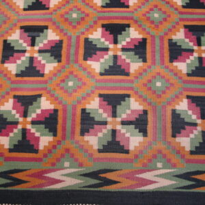 Flat weave rug with stepped geometric medallions in orange, sage green, magenta, and black.