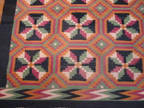 Flat weave rug with stepped geometric medallions in orange, sage green, magenta, and black.