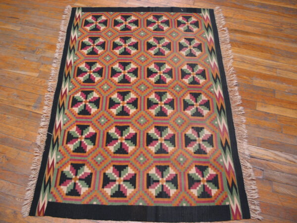 Colorful flatweave rug with repeating geometric squares and fringe rests on wooden planks.