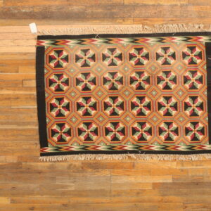 Geometric rug featuring repeating crosses and octagons in red, green, black, and gold on wood flooring.