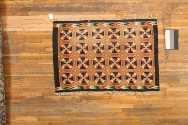 Geometric rug featuring repeating crosses and octagons in red, green, black, and gold on wood flooring.