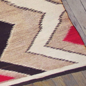 Flatwoven rug featuring bold zig-zags in cream, tan, black, and red on distressed wooden floor.