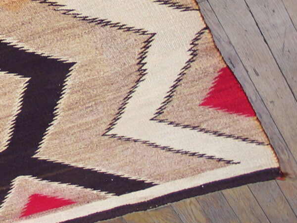 Flatwoven rug featuring bold zig-zags in cream, tan, black, and red on distressed wooden floor.