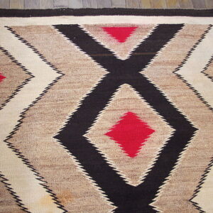 Low-pile rug featuring bold, serrated black, red, cream, and brown geometric diamonds on wood floor.