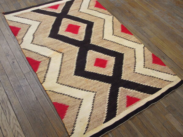 Flatweave rug with red, black, and neutral zigzags and diamonds rests on rustic hardwood flooring.
