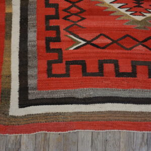 A red geometric flatweave rug with a striped border rests on distressed gray wood plank flooring.