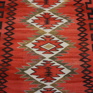 Red flatwoven rug featuring a central column of diamond patterns outlined in white and earthy tones.