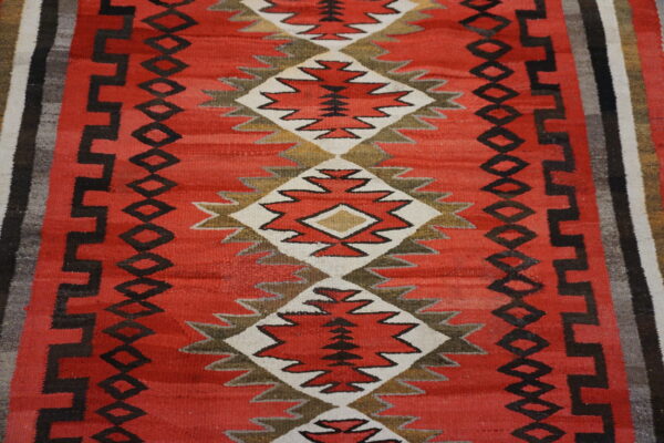 Red flatwoven rug featuring a central column of diamond patterns outlined in white and earthy tones.