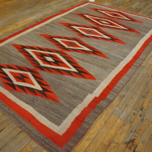 Flat-weave rug featuring large red and black geometric diamonds on a mottled gray background, resting on worn wood planks.